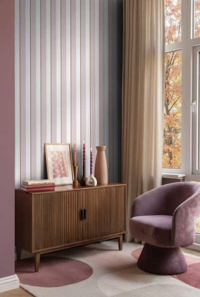 Wohnraum mit gestreifter Tapete, Holzkommode, Dekoration und Sessel.