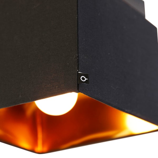 Eckige Leuchte mit schwarzem Stoffschirm, goldener Innenseite und sichtbarem Leuchtmittel.