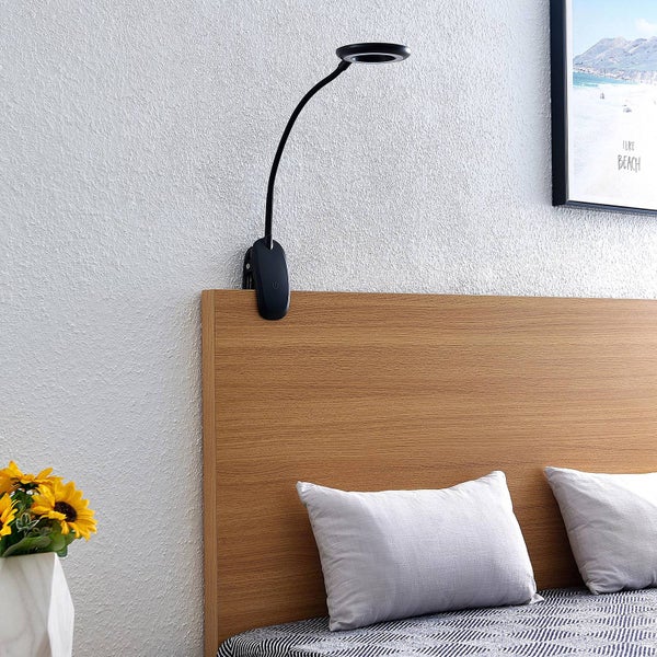 Schwarze LED-Klemmleuchte mit flexiblem Schwanenhals, am hölzernen Kopfteil eines Bettes befestigt.