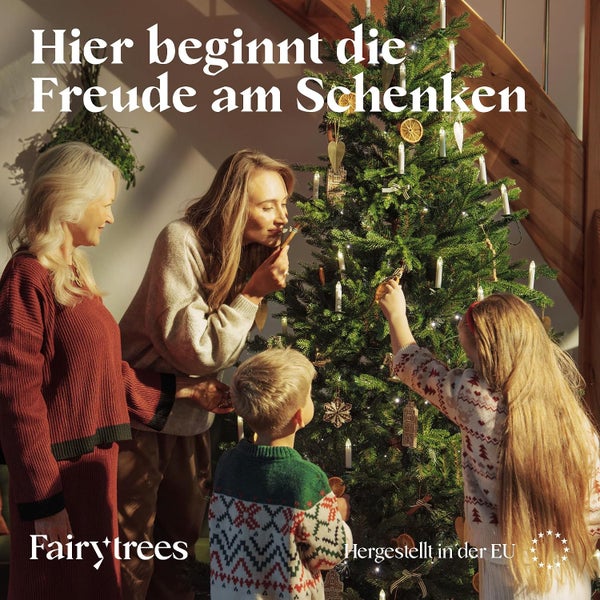Familie schmückt einen Weihnachtsbaum von Fairy Trees in einem Wohnzimmer, hergestellt in der Europäischen Union.