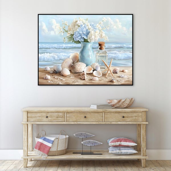 Wandbild mit maritimem Motiv von Blumen und Muscheln am Strand gerahmt über einer hölzernen Konsole mit Korb und Dekoration.