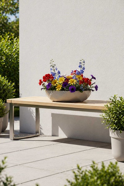 Bunte Blumenschale mit verschiedenen Sommerblumen auf einer modernen Gartenbank aus Holz und Metall.