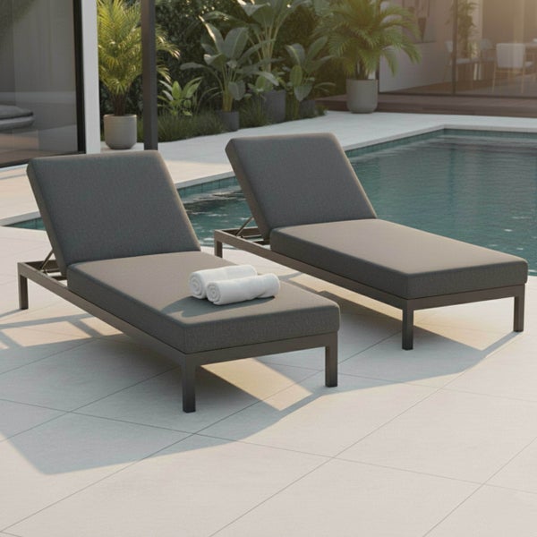 Zwei anthrazitfarbene Sonnenliegen mit Polstern und verstellbaren Rückenlehnen auf einer gefliesten Terrasse neben einem Pool.