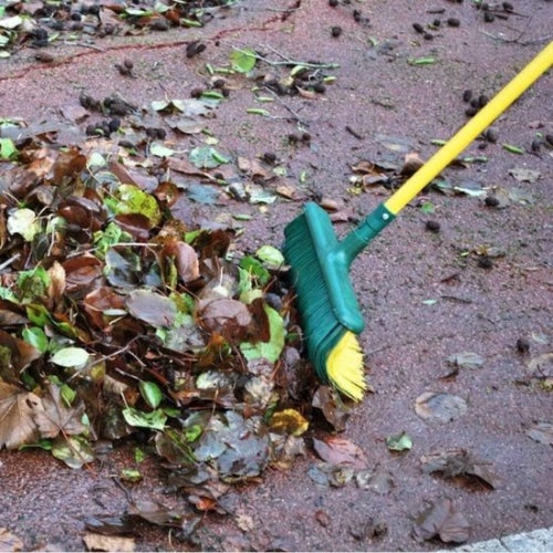 Besen kehrt Laub auf einer gepflasterten Fläche.