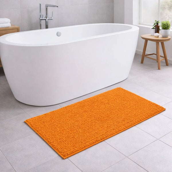 Moderner Badezimmerraum mit weißer freistehender Badewanne und einem rechteckigen orangefarbenen Badeteppich auf grauen Fliesen.