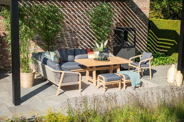 Garten-Lounge-Set aus Holz mit Ecksofa, Sessel und Tisch, graue Polster und Seilgeflecht, auf einer sonnigen Terrasse vor einer Backsteinmauer.