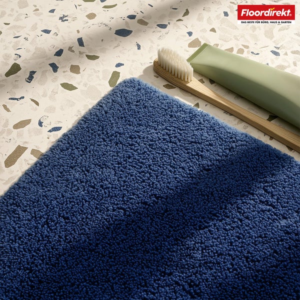 Blauer Badvorleger neben Bambuszahnbürste und Tube