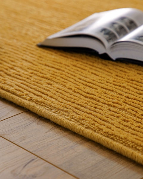 Teppich mit strukturierter Oberseite und Rippenmuster auf einem Holzfußboden mit einem aufgeschlagenen Buch.