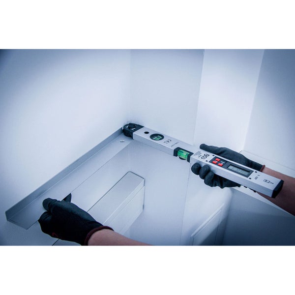 Eine Person mit Handschuhen verwendet eine digitale Wasserwaage an einer Badezimmerinstallation.