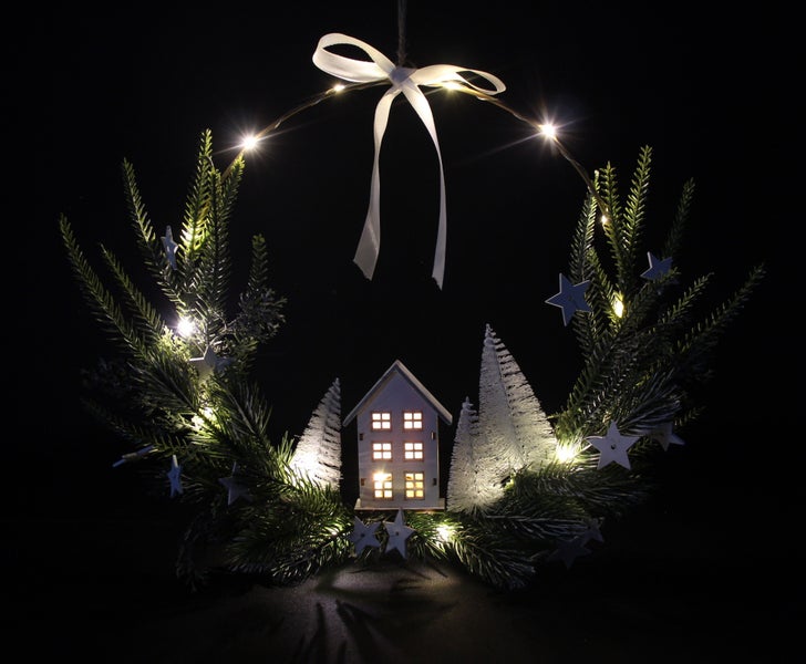 Weihnachtlicher Türkranz mit LED-Beleuchtung, Zierschleife, Sternen und einem dekorativen Haus