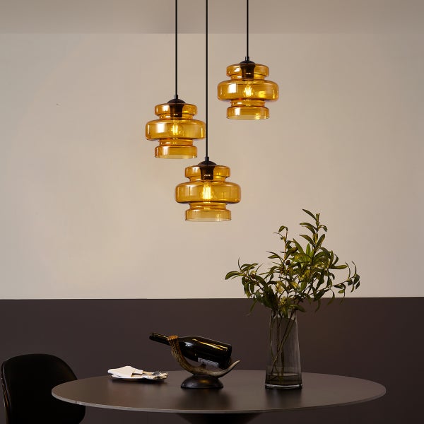 Szene mit drei Pendelleuchten aus Glas über einem Esstisch mit Dekoration