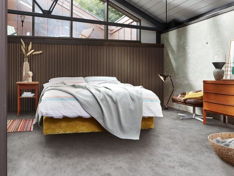 Modernes Schlafzimmer mit Boxspringbett vor einer Holzwand mit Lamellenverkleidung, Betonboden und großen Dachfenstern im Industriedesign.