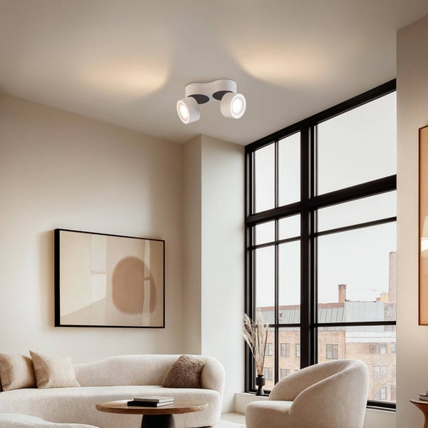 Modernes Wohnzimmer mit zweiflammigem Deckenstrahler, minimalistischen Möbeln, großen Fenstern und heller, strukturierter Atmosphäre.