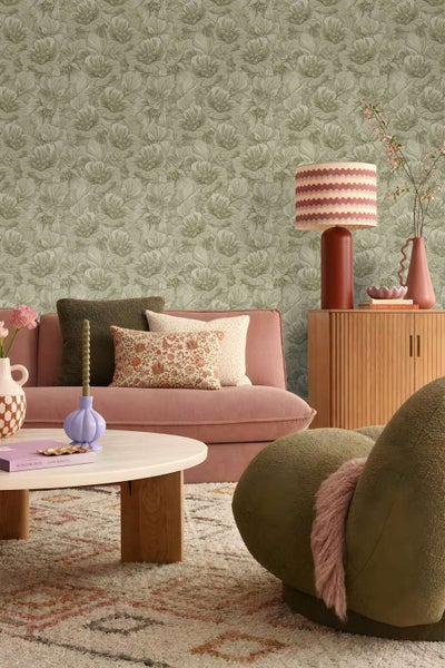 Wohnzimmer mit florale Mustertapete, rosa Sofa, Holzkommode und moderner Dekoration in einem wohnlichen Ambiente.