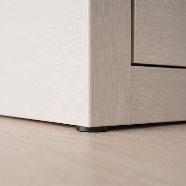 Detailansicht der Ecke eines hellen Holzmöbels mit einem kleinen schwarzen Möbelgleiter auf einem Boden.