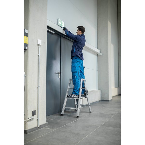 Handwerker montiert ein Notausgangsschild auf einer Leiter