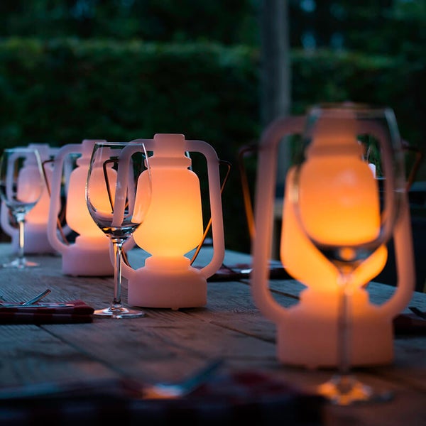 Beleuchtete LED-Laternen in klassischer Form auf einem Holztisch im Freien mit Weingläsern und Besteck.