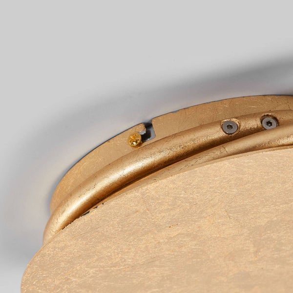 Nahaufnahme einer goldfarbenen Deckenleuchte mit Montageschrauben und strukturierter Oberfläche in Blattgold-Optik.