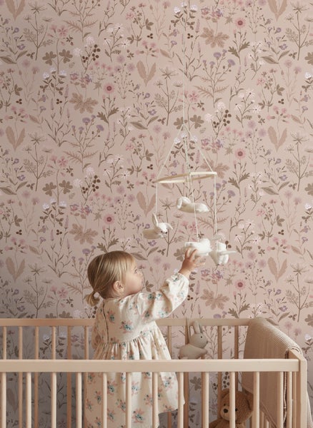 Vliestapete mit Wildblumenmuster in einem Kinderzimmer mit Holzgitterbett und einem Kind, das nach einem Mobile greift.