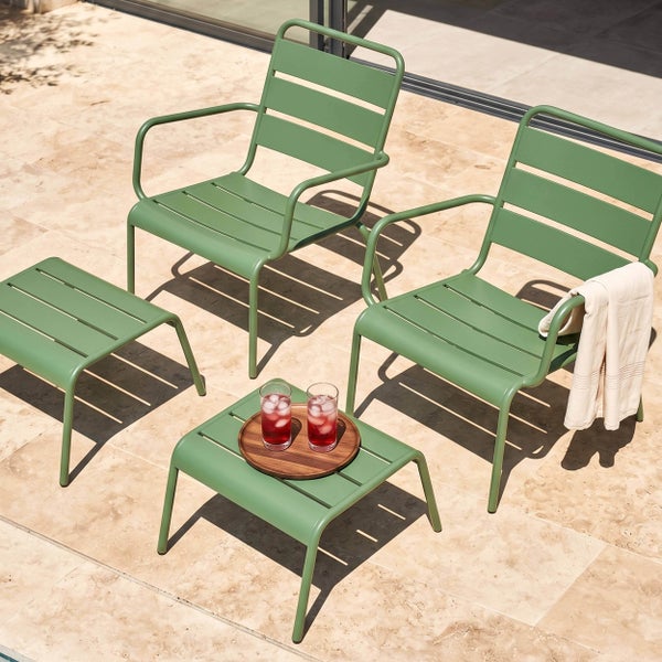Grünes Gartenmöbel-Set aus Metall mit zwei Sesseln und zwei Beistelltischen im Latten-Design auf einer hellen Steinterrasse.