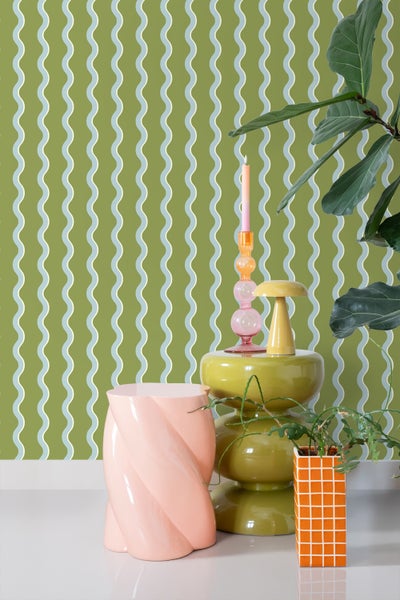 Dekorative Szene mit einem Beistelltisch, einem Kerzenständer, einer Blumenvase und einer Zimmerpflanze vor einer gemusterten Tapete.