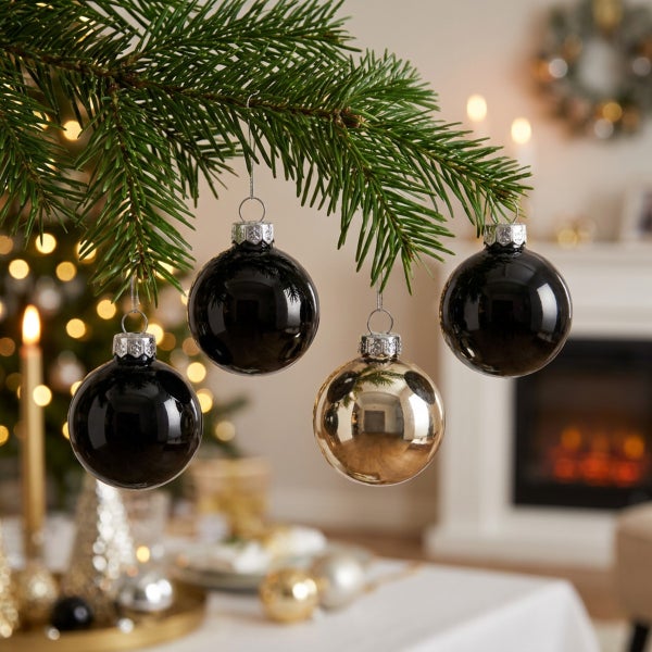 Drei Weihnachtskugeln hängen an einem Tannenzweig vor einem unscharfen Hintergrund mit Lichtern.