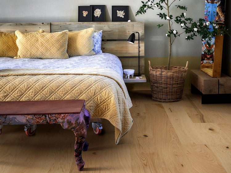Holzparkett in einem hellen Schlafzimmer mit rustikalem Holzbett, einem geflochtenen Korb und einer verzierten Bank.
