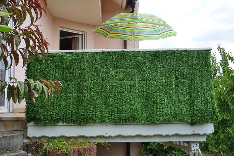 Balkon mit künstlicher Hecke und Ausblick auf eine grüne Landschaft