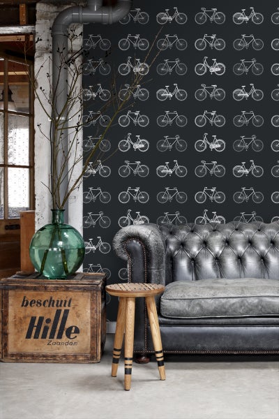 Dekorative Szene mit einer Couch, einem Hocker und einer Holzkiste vor einer Wand mit Fahrradmuster.