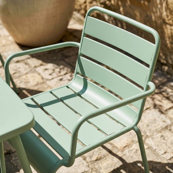 Gartenstuhl aus Metall mit Armlehnen und Latten-Design auf einer Steinterrasse.