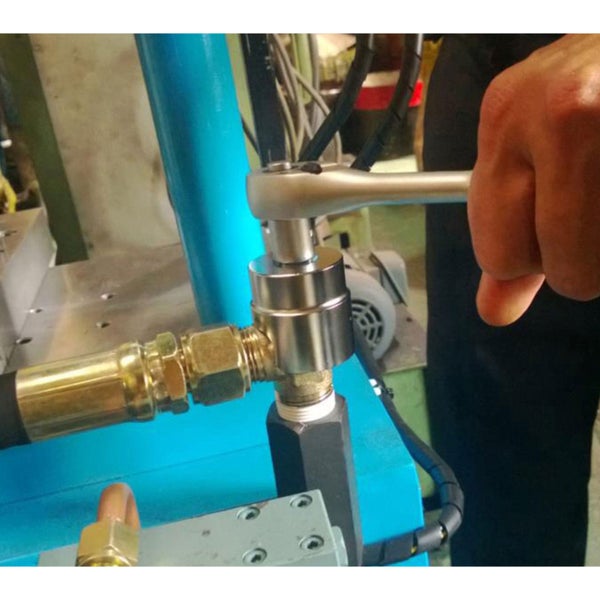 Hand bedient eine Ratsche an einer metallischen Rohrverbindung einer Maschine.