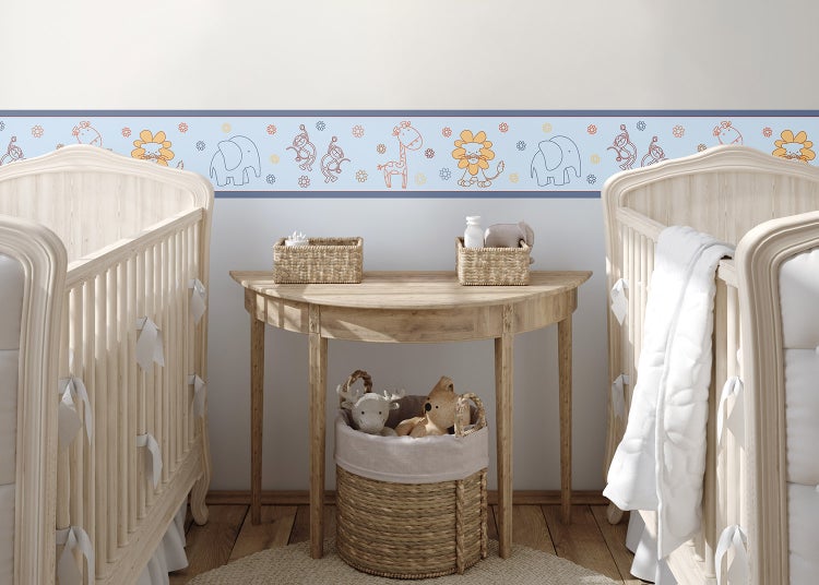 Wandbordüre mit Safaritieren wie Elefanten, Löwen und Giraffen in einem hellen Kinderzimmer mit zwei hellen Holzgitterbetten und Beistelltisch.
