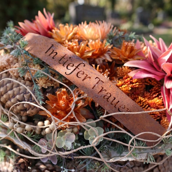 Grabgesteck mit Edelrostband und der Aufschrift In tiefer Trauer dekoriert mit Herbstblumen und Zapfen für die Grabdekoration.