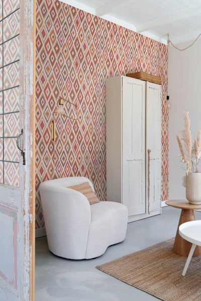 Wohnzimmer mit gemusterter Tapete, Sessel und Holzschrank