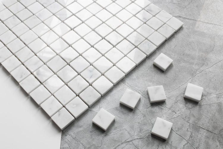 Quadratische Mosaikfliesen aus weißem Marmor mit grauer Maserung und einzelne lose Mosaiksteine.