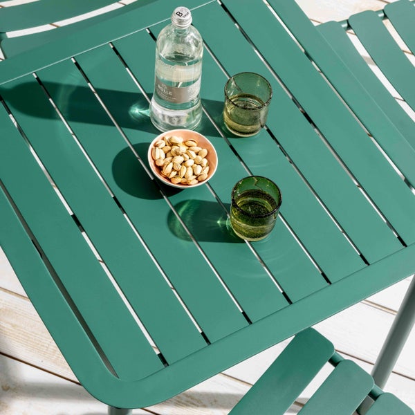 Moderner Gartentisch aus grünem Metall mit Lattenoberfläche und passenden Stühlen auf einer Holzterrasse.