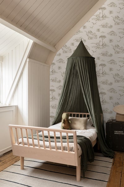 Helles Kinderzimmer mit Holzbett, Baldachin und Dinosaurier-Tapete.