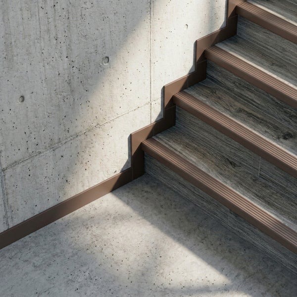 Treppenkantenprofil und Sockelleiste an einer Treppe in Holzoptik vor einer Sichtbetonwand.
