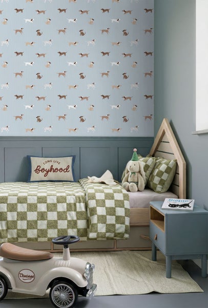 Tapete mit Hundemotiv in einem Kinderzimmer über einer dunklen Wandtäfelung, Bett mit karierter Decke und hölzernem Kopfteil in Hausform.