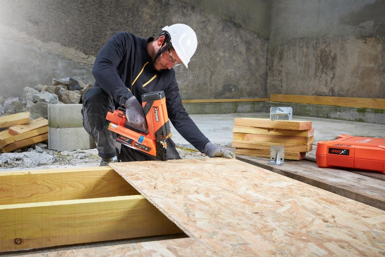 Handwerker mit Schutzhelm verwendet Paslode Gasnagler IM90Xi zur Befestigung einer Holzplatte auf einer Baustelle