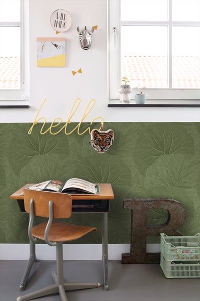 Ein Kinderzimmer mit Schreibtisch, Stuhl und Blattmuster-Tapete.
