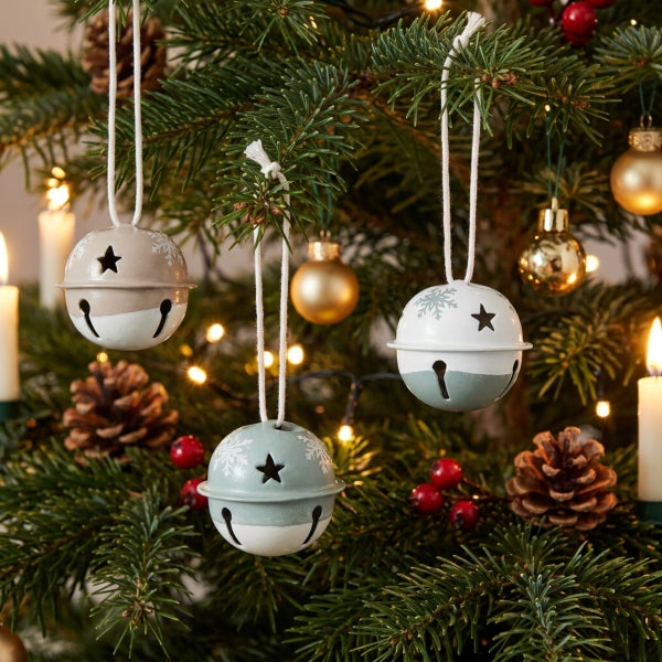 Drei hängende Metallglocken als Weihnachtsbaumschmuck mit Sternenmotiven und Schneeflocken an einem geschmückten Tannenbaum.