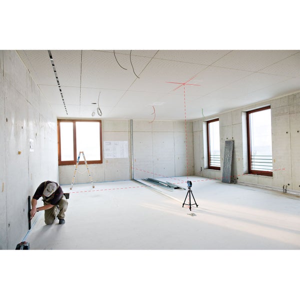 Innenaufnahme eines Raumes im Rohbau mit Handwerker, Leiter und Nivelliergerät mit Laser