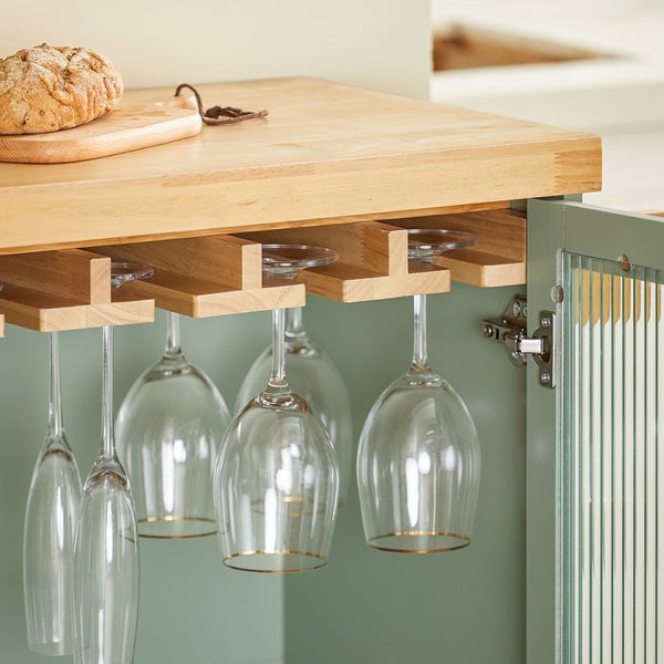 Weingläser hängen an einem hölzernen Gläserhalter unter einem Tresen. Ein Brot und ein Schneidebrett befinden sich auf dem Tresen.