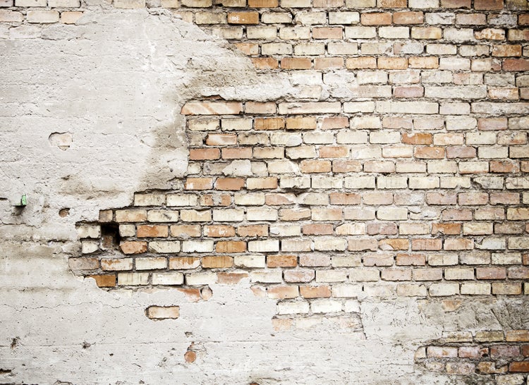 Alte Backsteinwand mit teilweise abgeplatztem Putz und freiliegendem Mauerwerk.