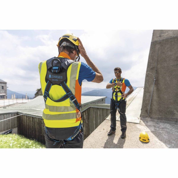 Zwei Personen in einem Zarges Salvex+ Auffanggurt mit integrierter Warnweste auf einem Dach in einer Berglandschaft.