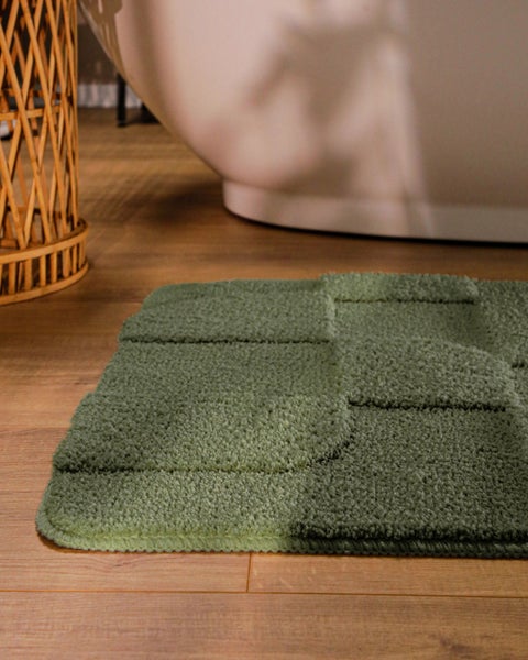 Quadratischer Badteppich mit Reliefstruktur vor einer Badewanne auf einem Holzboden.