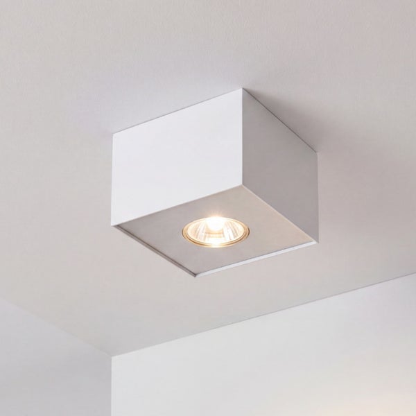 Quadratischer Aufbaustrahler in Weiß an der Decke montiert mit eingeschaltetem Leuchtmittel und warmem Licht.