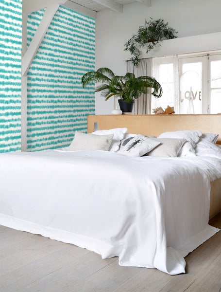 Helles Schlafzimmer mit weißer Bettwäsche, gemusterter Tapete und Zimmerpflanzen