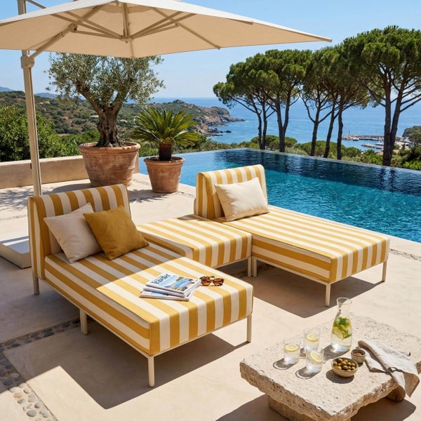 Hell gestaltete Terrasse mit moderner Gartenlounge am Pool, gelb-weiß gestreiften Polsterliegen, einem Sonnenschirm und weitem Meerblick.